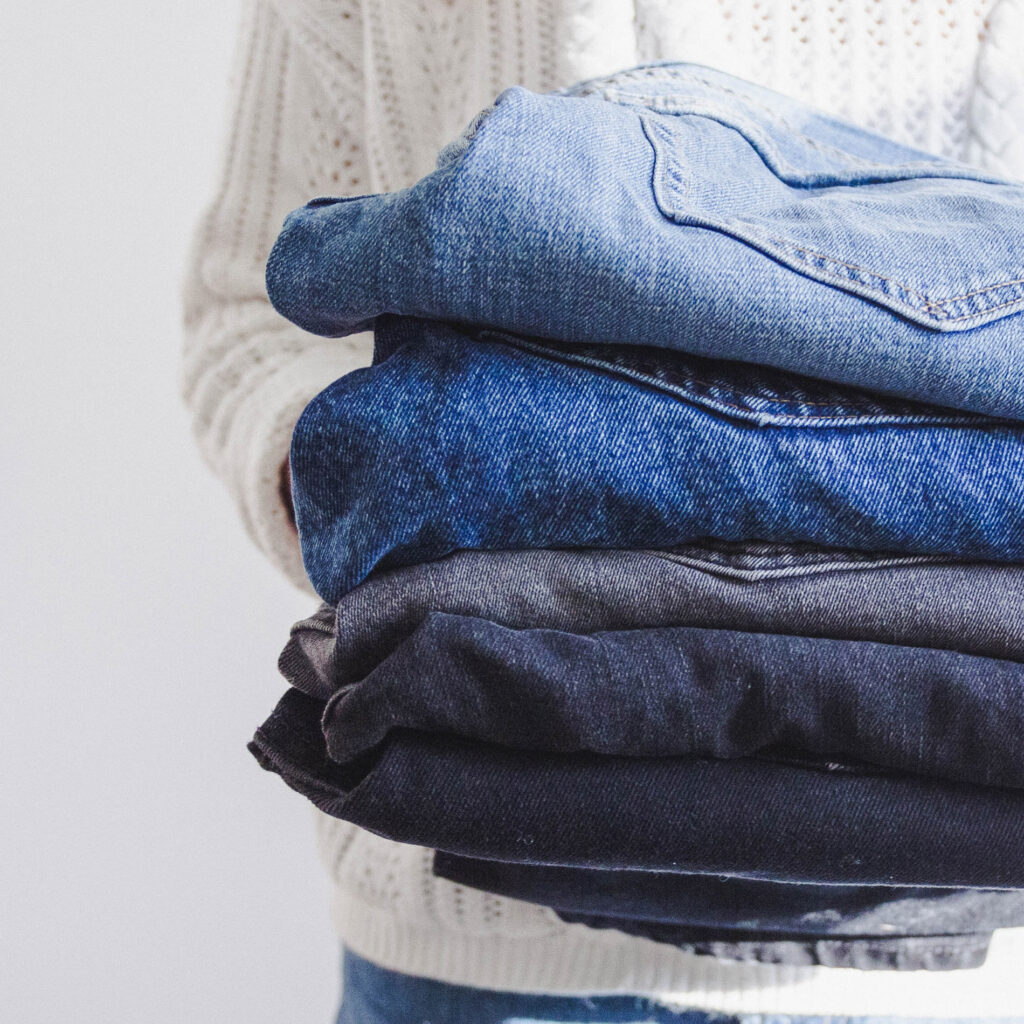 Person holding a stack of denim jeans.